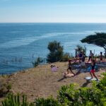 Camping Castels Les Criques de Porteils Gaeste entspannen beim Yoga im Schatten am Strand mit Blick auf das Mittlmeer 150x150