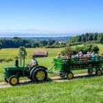 Camping Wirthshof Gaeste mit Kindern beim Ausflug in einem Traktoranhaenger durch die Landschaft mit Blick auf den Bodensee 150x150