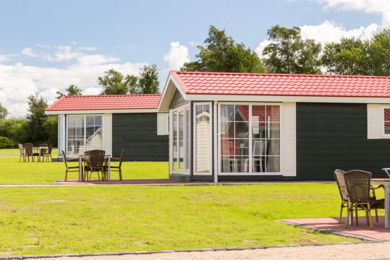 Ostseecamping Familie Heide auf einer Wiese gelegene moderne Mietunterkuenfte mit grosser Fensterfront und einer gepflasterten Terrasse mit Stuehlen und einem Tisch 4c807455 014a 4b77 986b f2bbc9ba624d 768x512