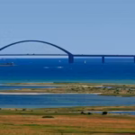 Camping Fluegger Strand Strand in der Naehe des Campingplatzes mit Bruecke in der Ferne  150x150