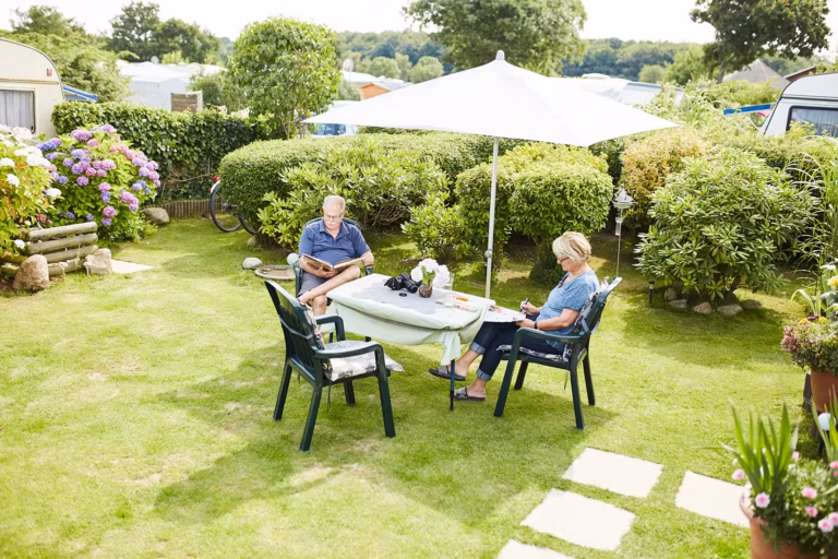 Ostsee Freizeitpark Booknis Gaeste vom Campingplatz sitzen unter dem Sonnenschirm auf dem Rasen 768x512