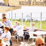Ostsee Freizeitpark Booknis Veranda von dem Restaurant mit Sonnenschirmen mit Blick auf das Meer auf dem Campingplatz 150x150
